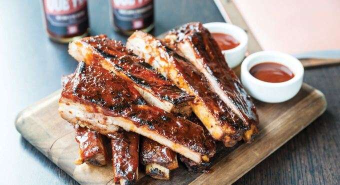 Sliced pork ribs on a board with ketchup and BBQ sauce