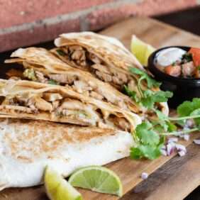 Sliced quesadilla wedges served with lime and salsa on a board