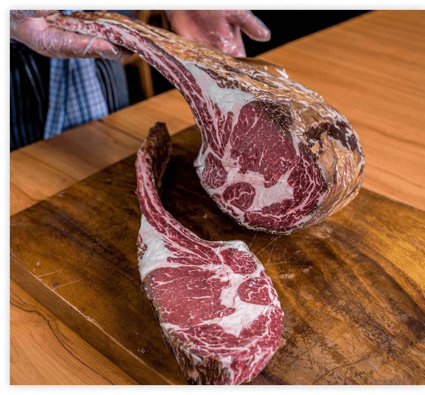 Raw dry-aged tomahawk steaks on a wooden board