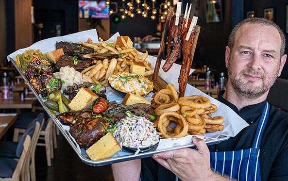Chef holding a BBQ meat platter with ribs, brisket and onion rings