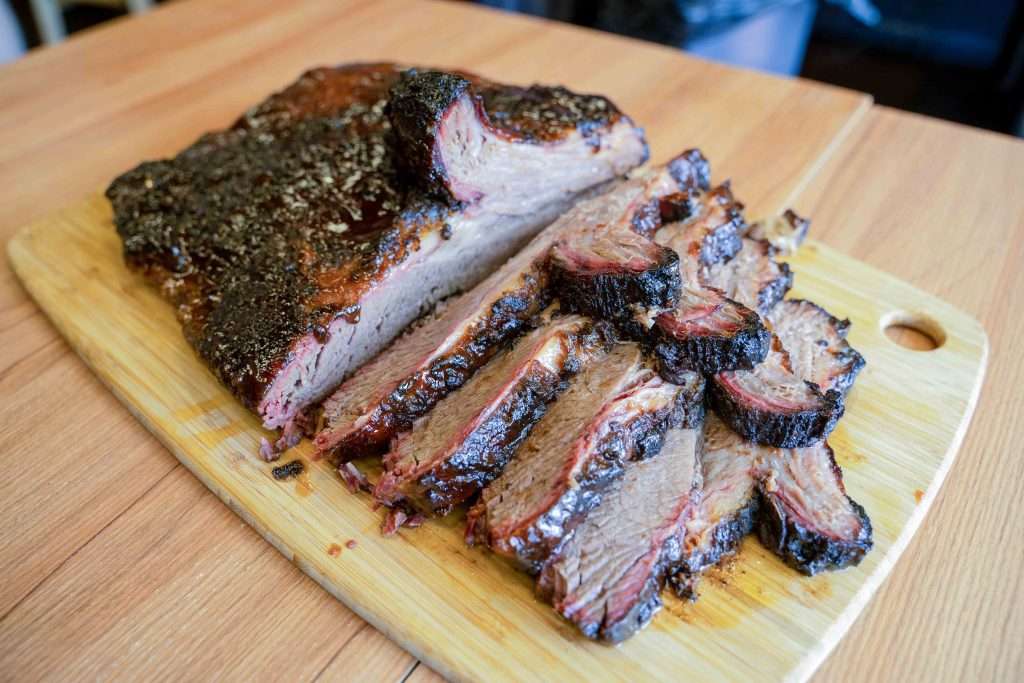 Sliced smoked beef brisket with a peppery bark on a board