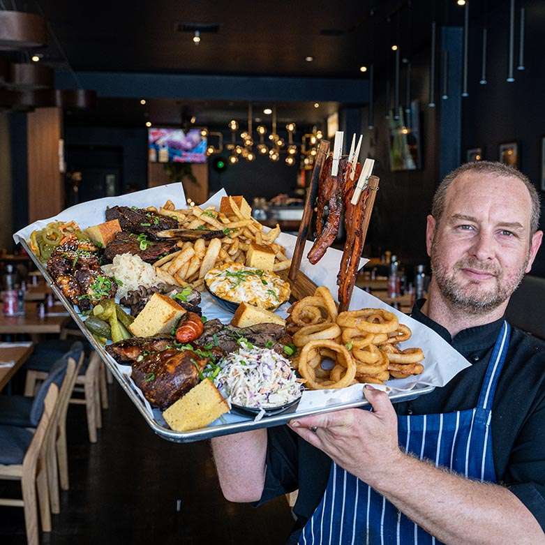 Chef holding a BBQ meat platter with ribs, brisket and onion rings