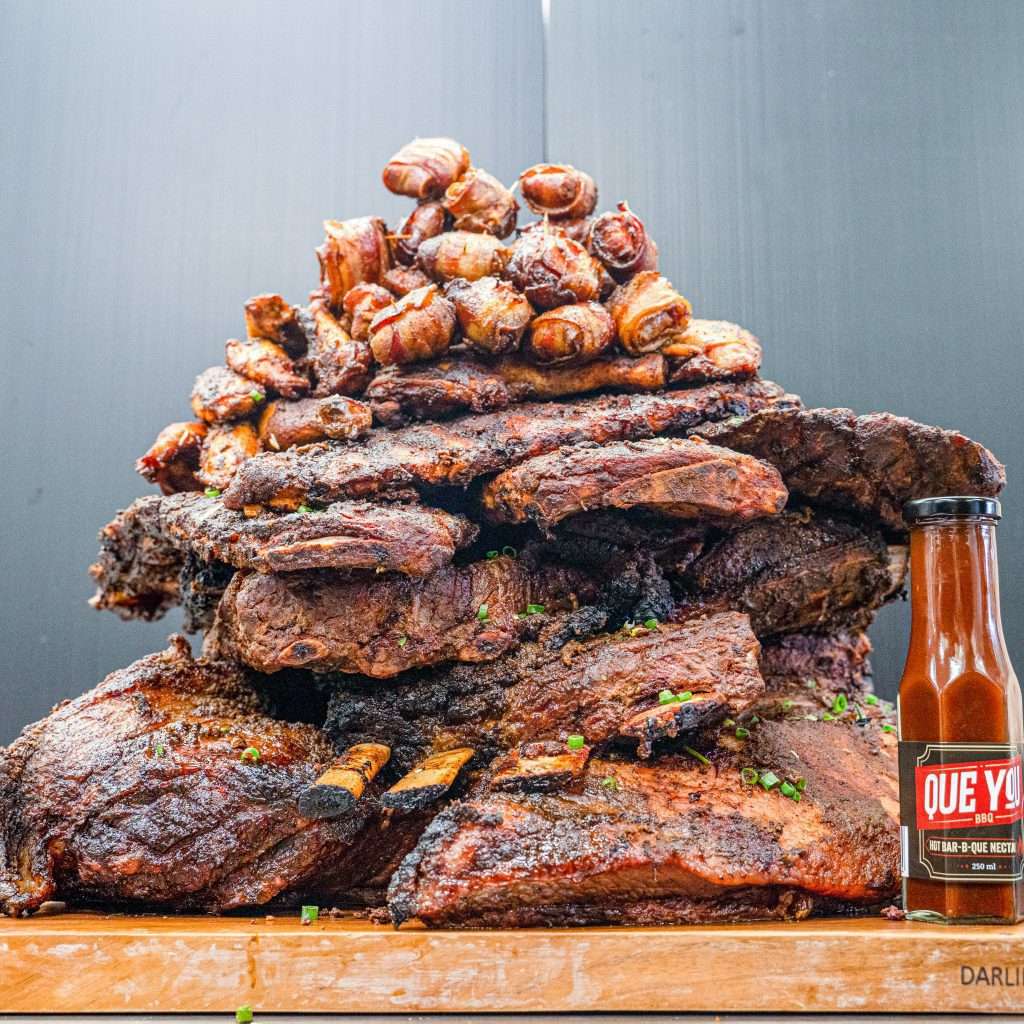 Meat Mountain: a towering stack of smoked ribs and meats beside a hot sauce bottle
