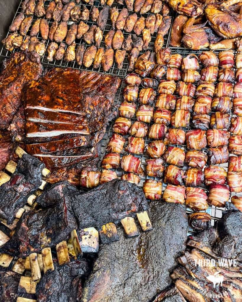 Smoked meats and bacon-wrapped bites laid out on a barbecue smoker grate