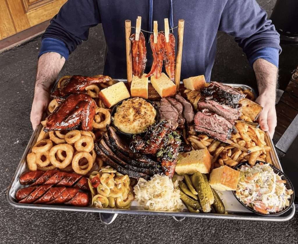 Guest presenting a large BBQ meat platter with ribs, wings and sides for six