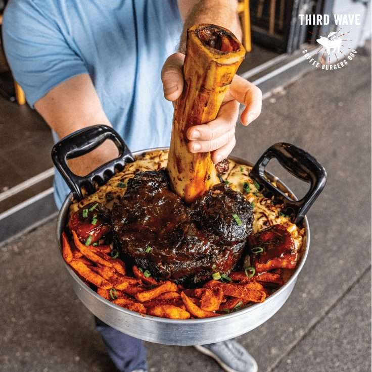 Guest holding Thor's Hammer whole smoked beef shin in loaded fries