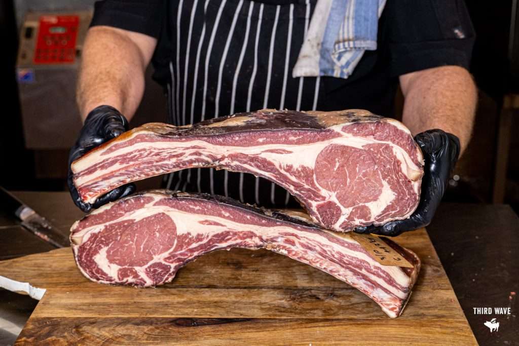 Butcher holding two tomahawk steaks on a wooden board