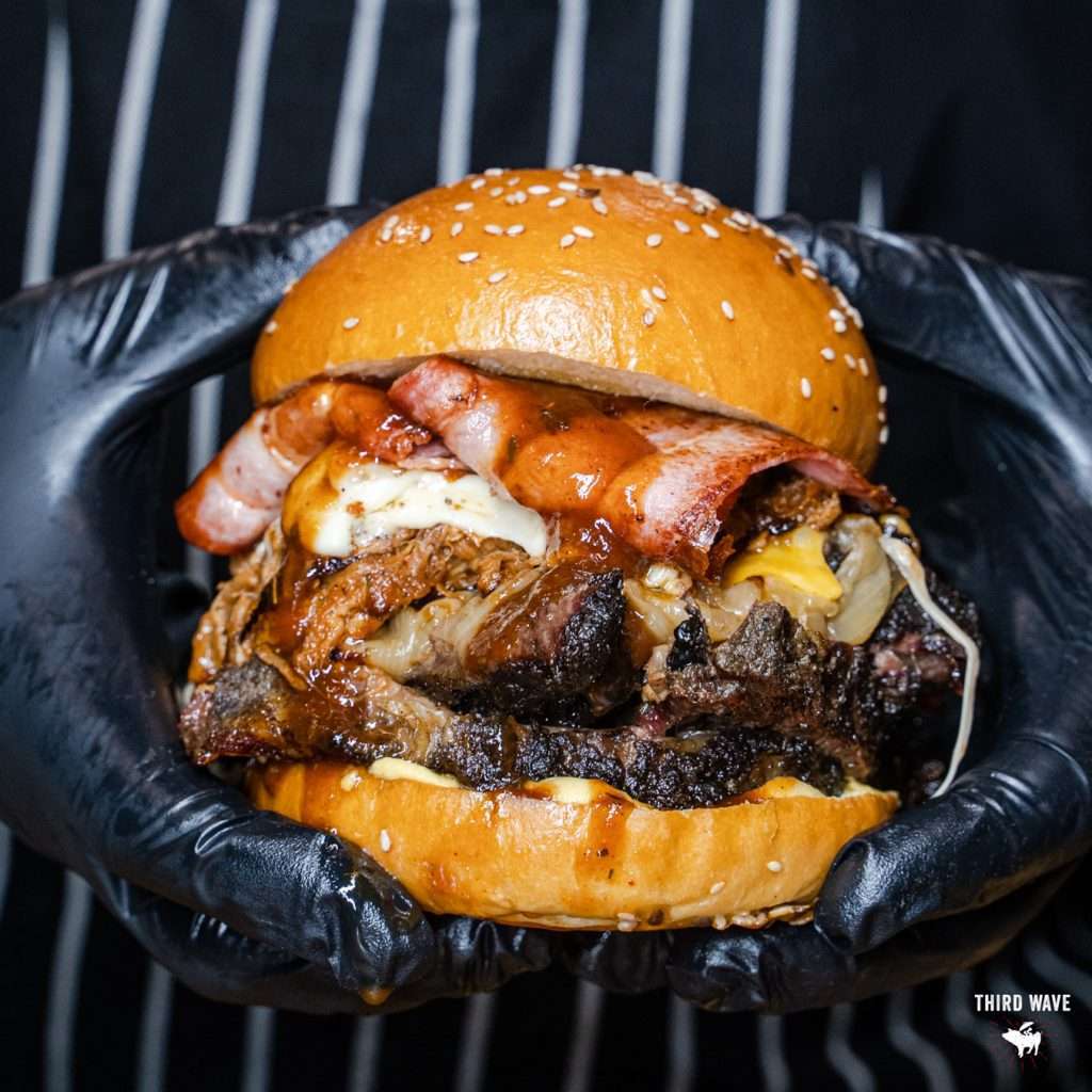 Oh Mamma burger held close-up with bacon and melted cheese