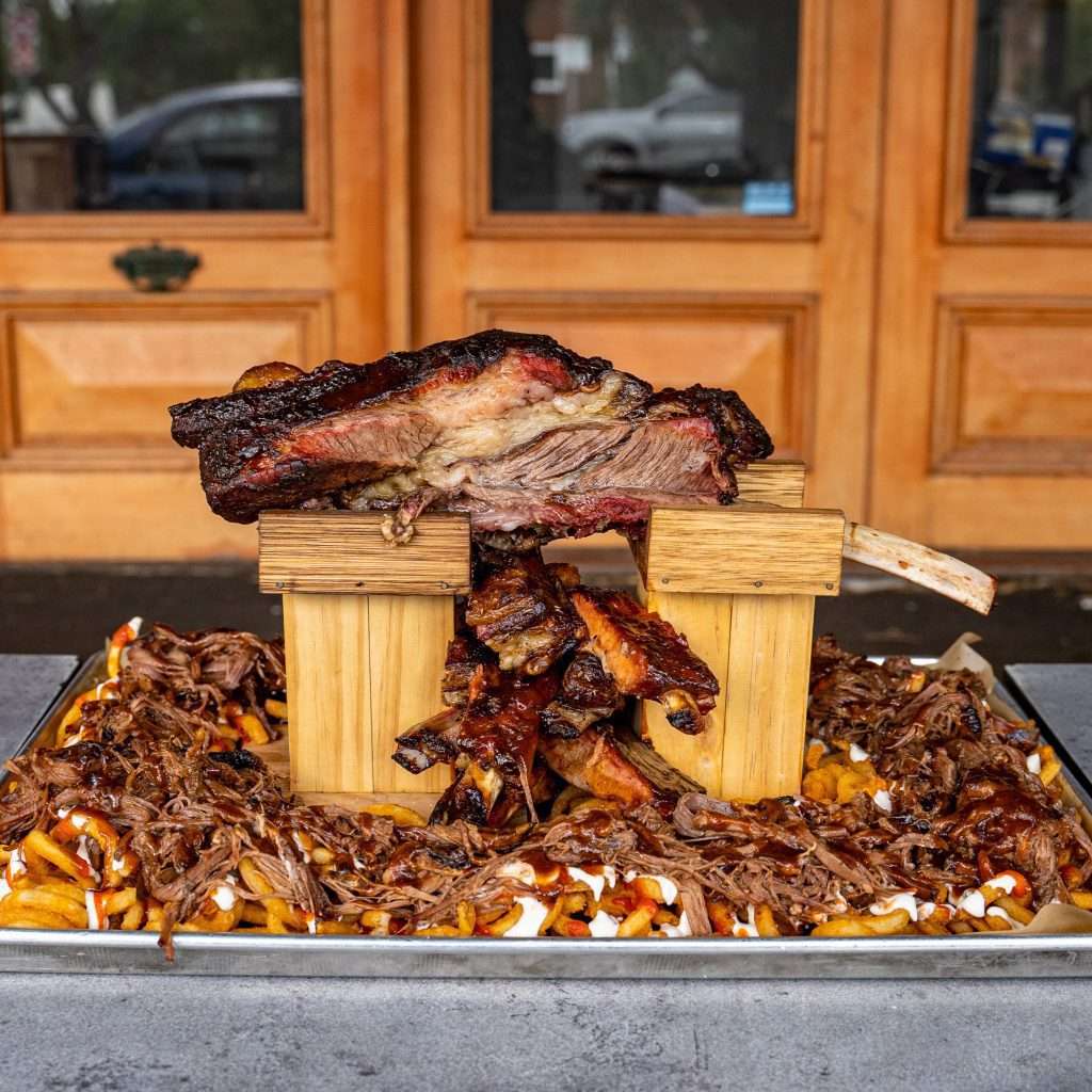 Rack of ribs displayed on a stand over pulled meat and fries