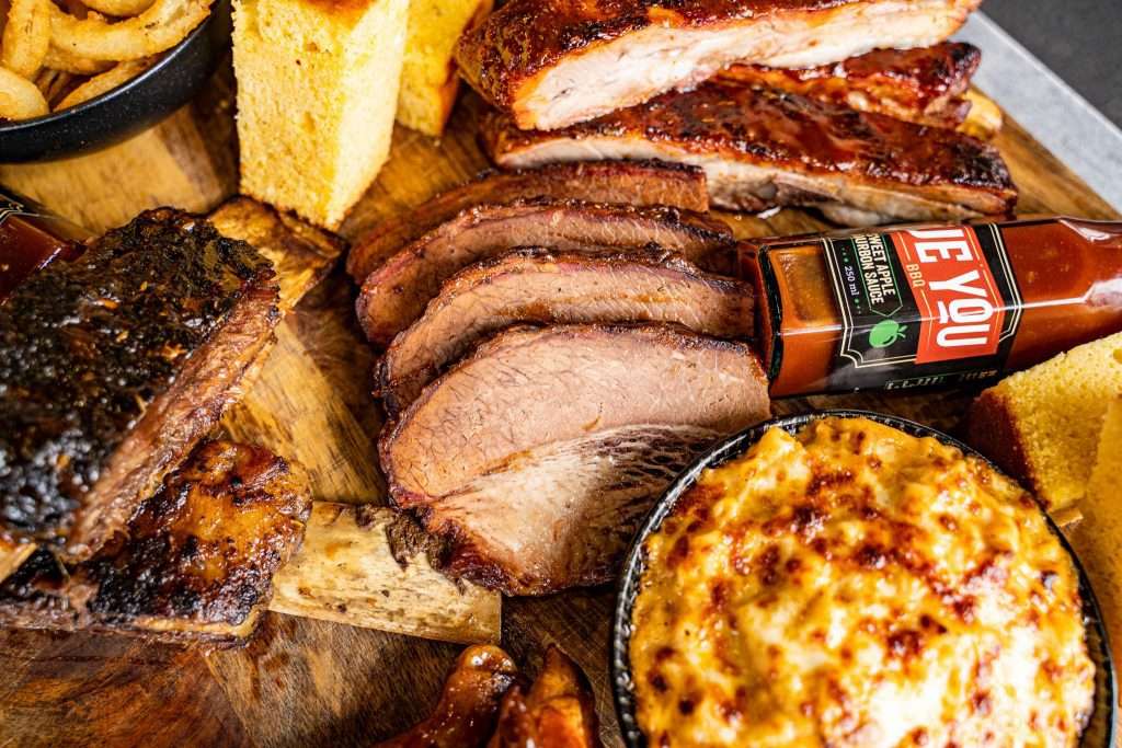 Sliced smoked brisket with mac and cheese, cornbread and BBQ sauce
