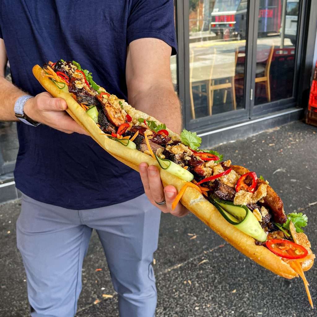 Guest holding Australia's largest banh mi baguette with pickled veg and chilli