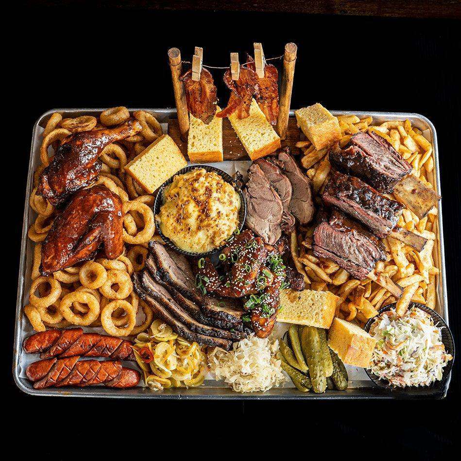 Large BBQ meat platter with whole chicken, ribs, brisket and sides, overhead view