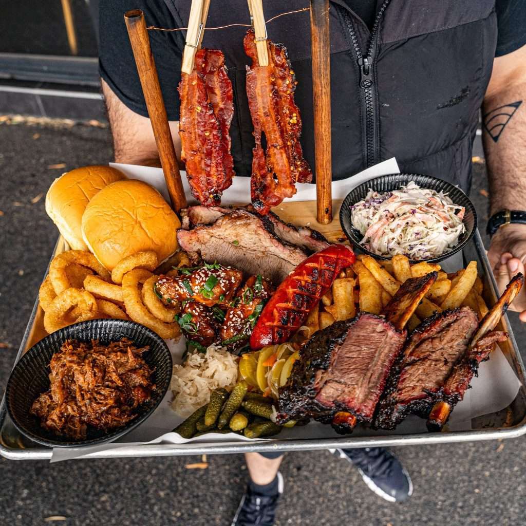 Large BBQ meat platter with ribs, brisket and coleslaw, being carried