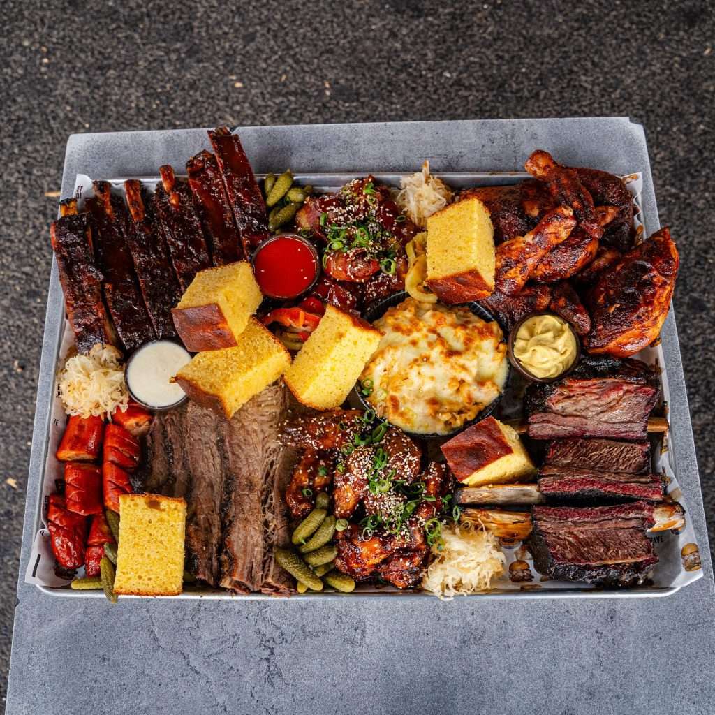Large BBQ meat platter with ribs, brisket, sausages and cornbread, overhead view
