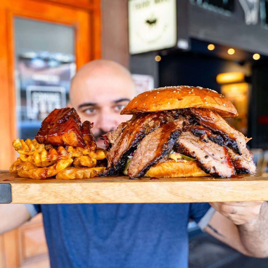 Guest holding a board with the Brisket Overloaded Oh Daddy Burger and fries