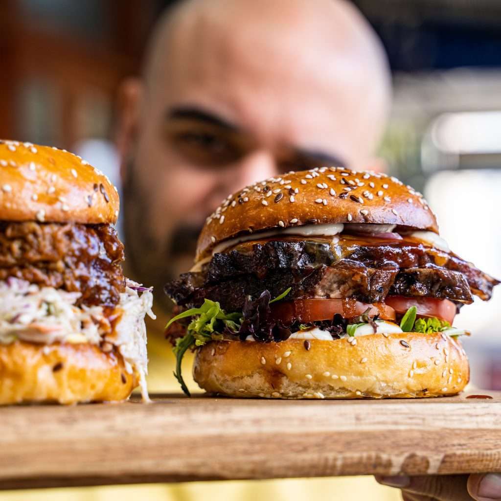 Two stacked charcoal-grilled burgers on a wooden board