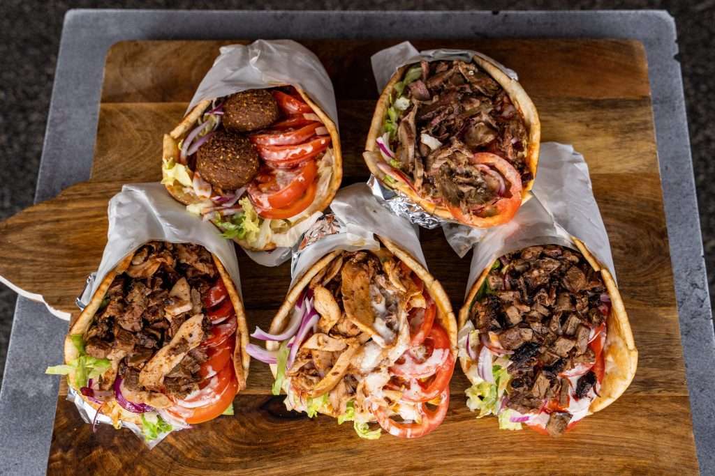 Five kebab wraps filled with meat and salad on a board