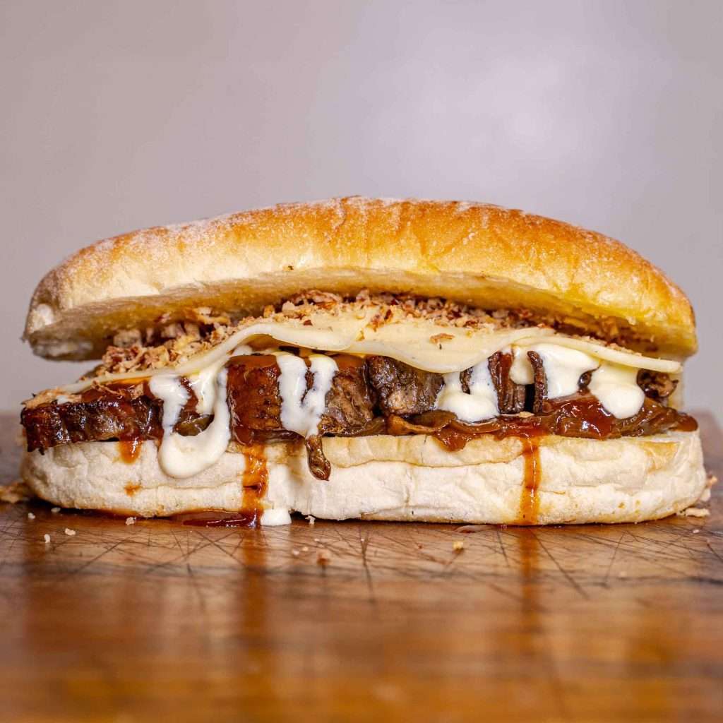 Sliced brisket sandwich with sauce drizzle, cut in half