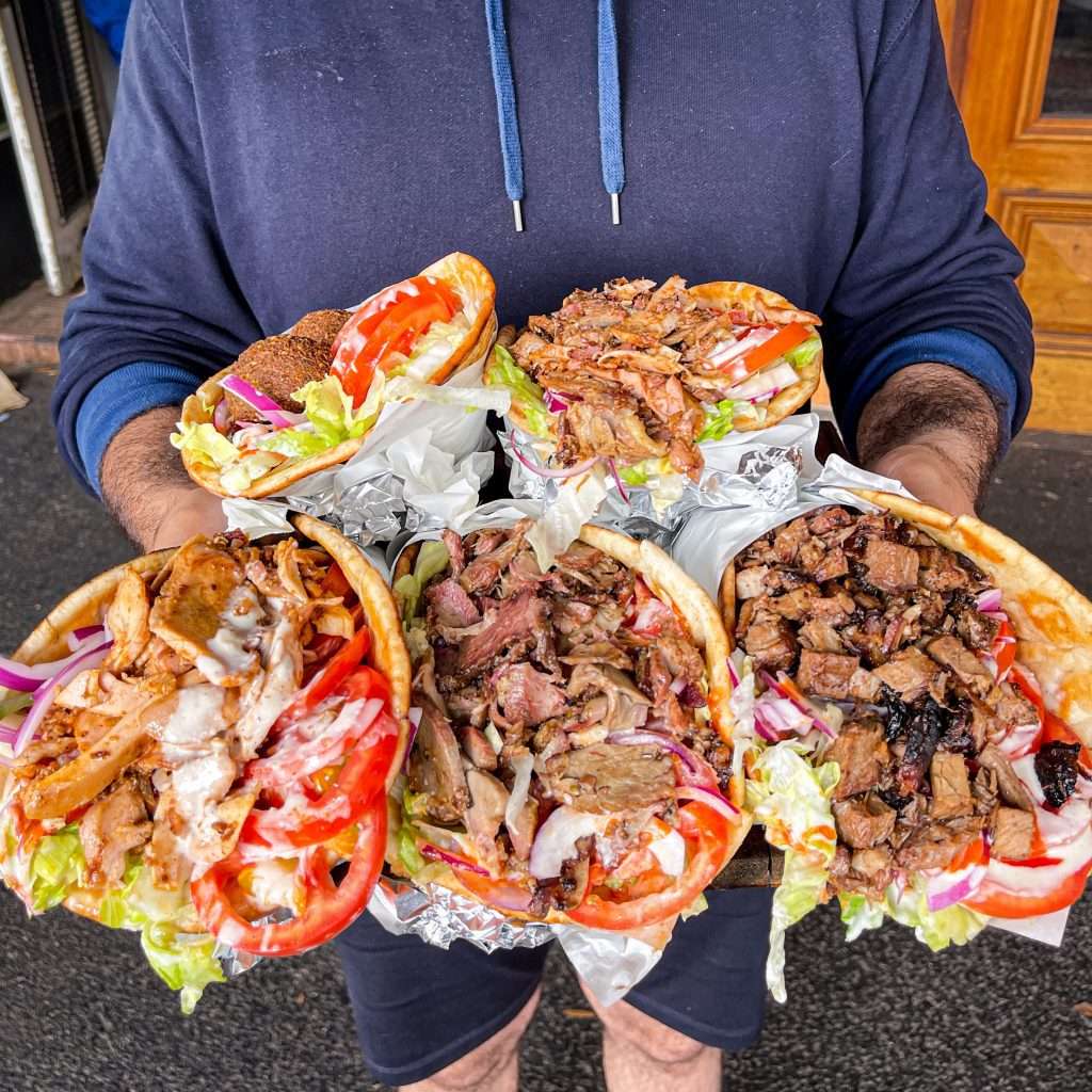 Person holding three kebab wraps filled with meat and salad