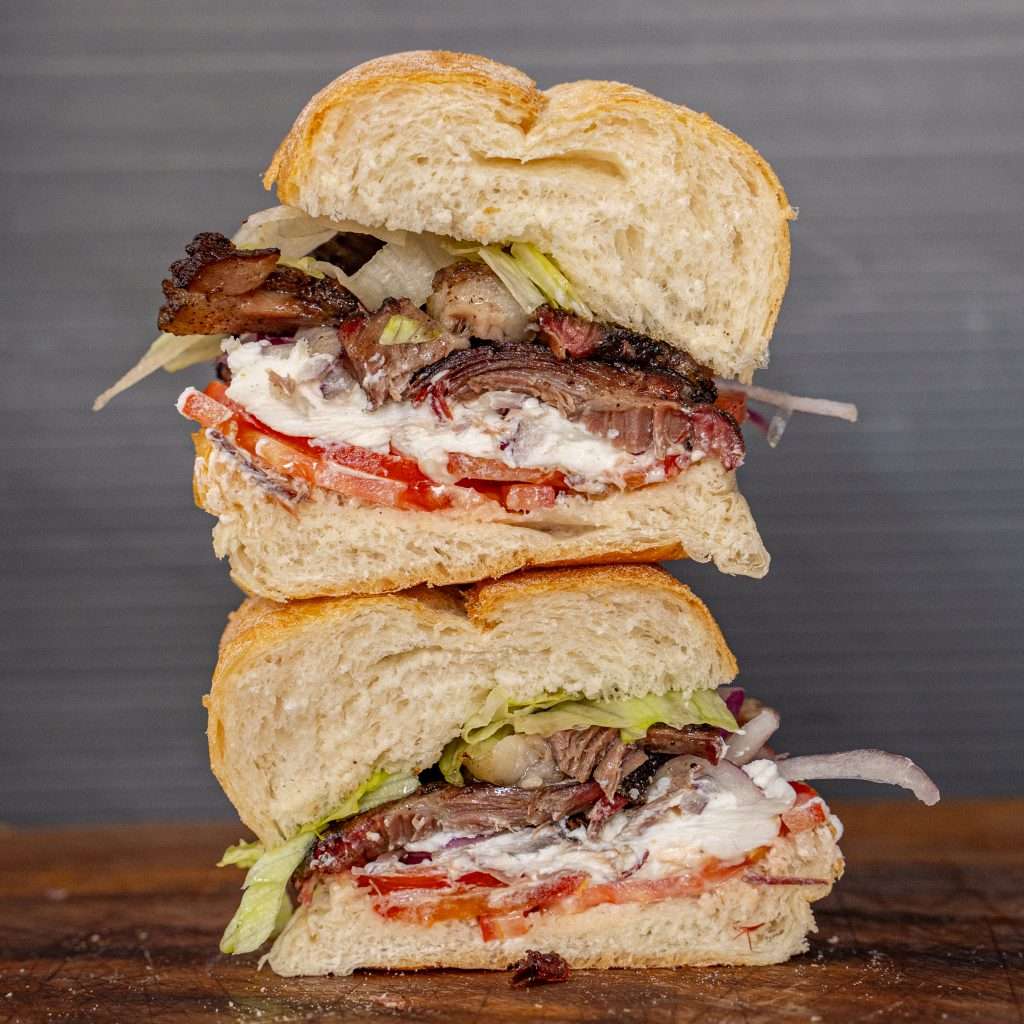 Sando Deli sandwich stacked with meat, tomato and lettuce