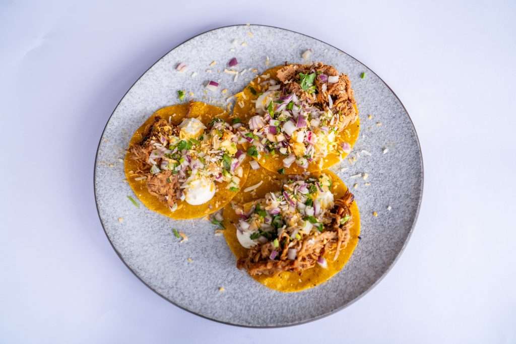 Three tacos topped with pulled meat and herbs on a plate