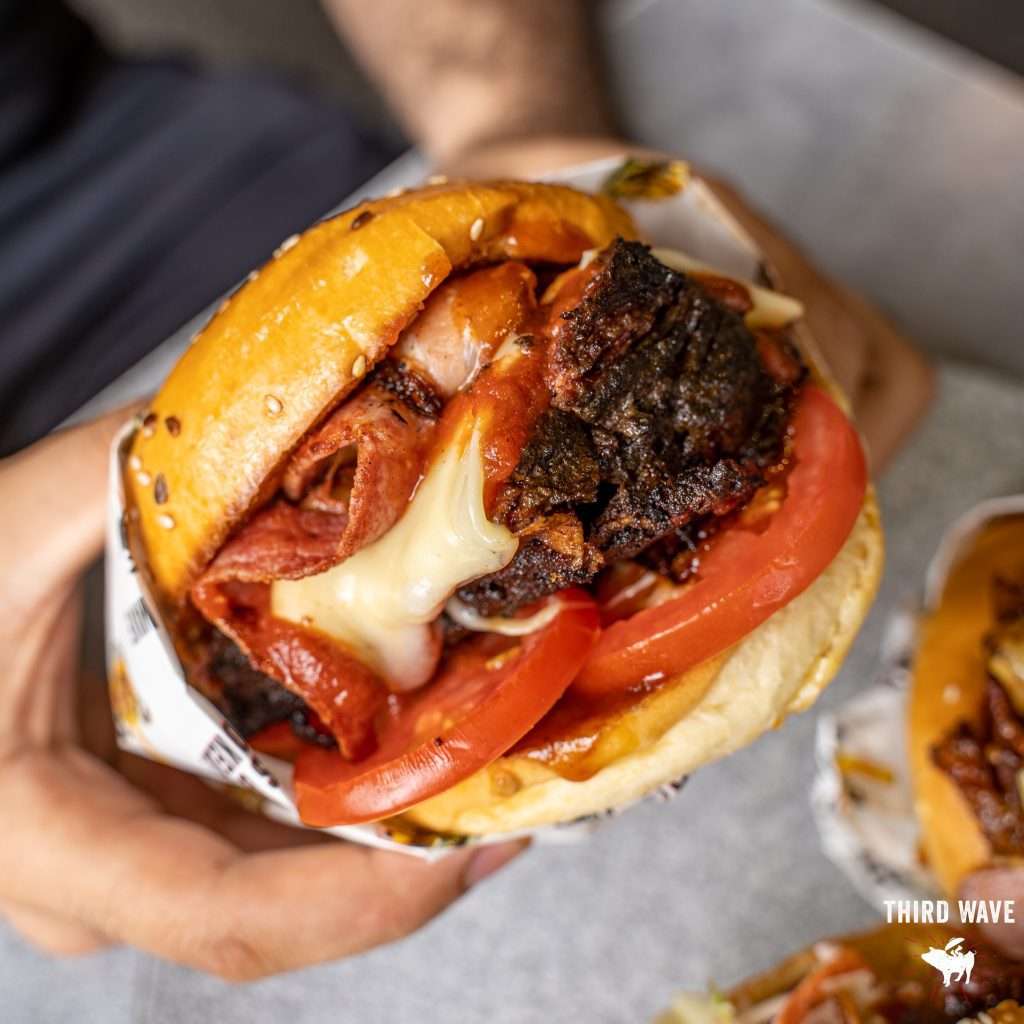 Burger with bacon, cheese and tomato held in a bread roll