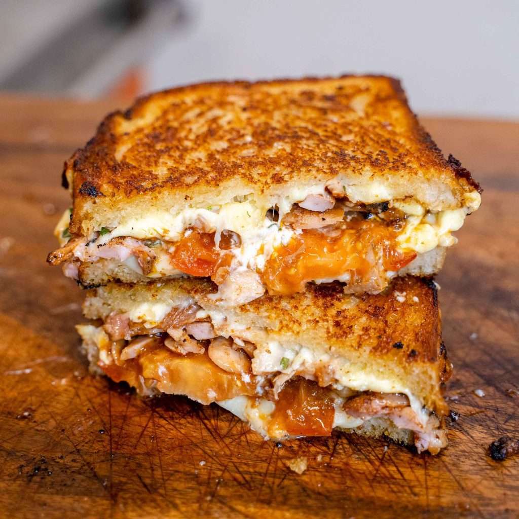 Smoked chicken toastie halves on a board, cheese melting out