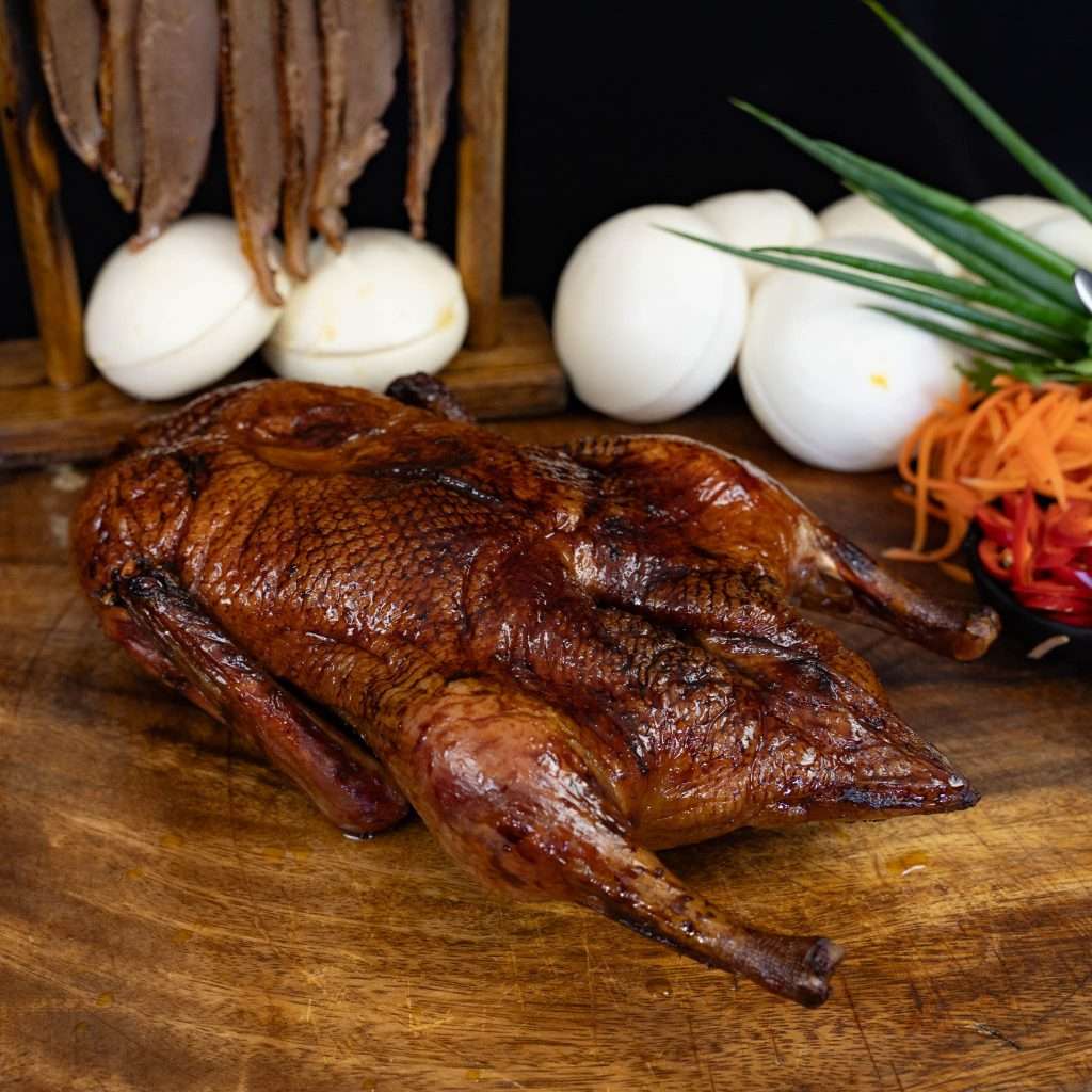 Whole smoked duck on a board with steamed bao buns