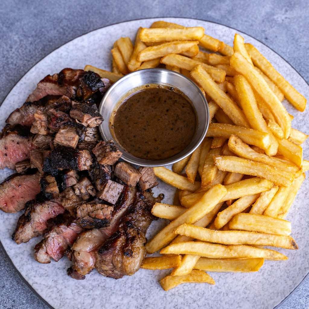 Steak bites arranged around a pot of gravy with fries