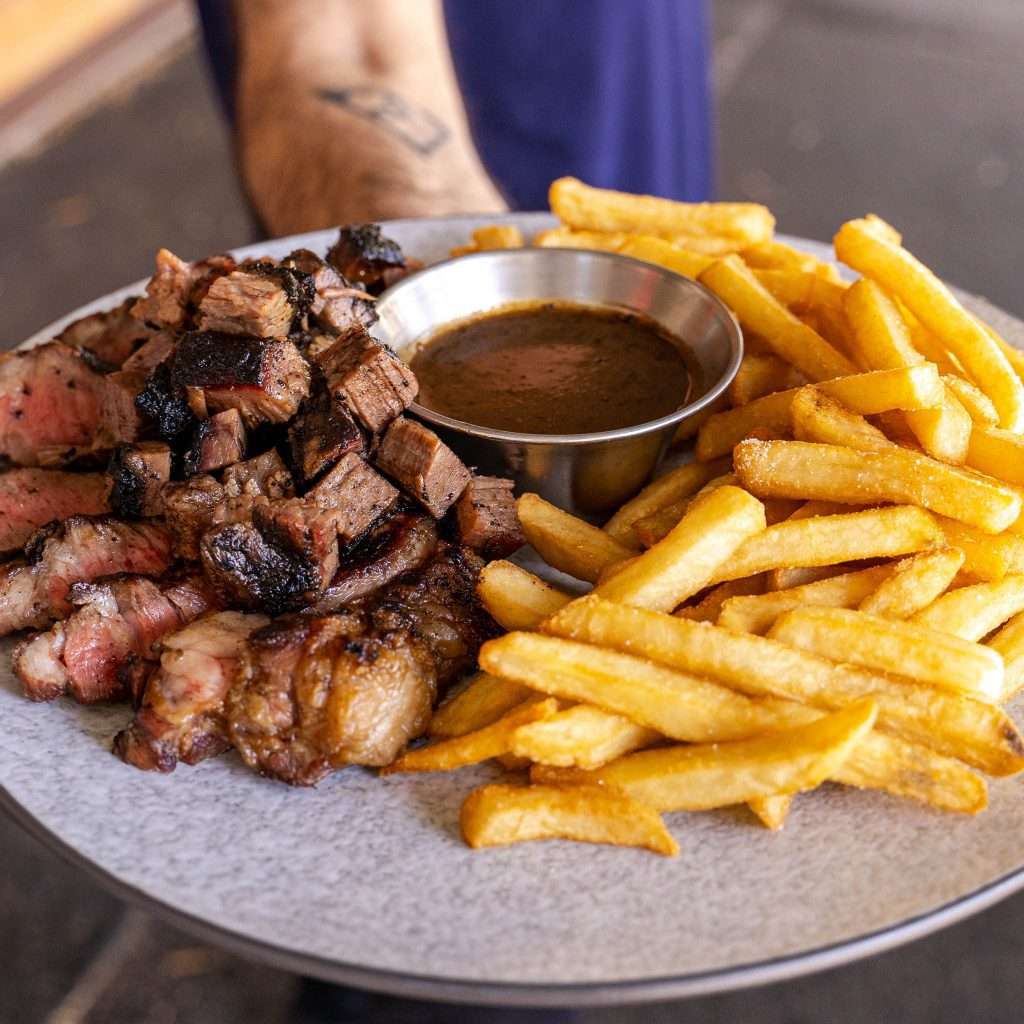 Plate of steak bites and fries with a pot of gravy, held out