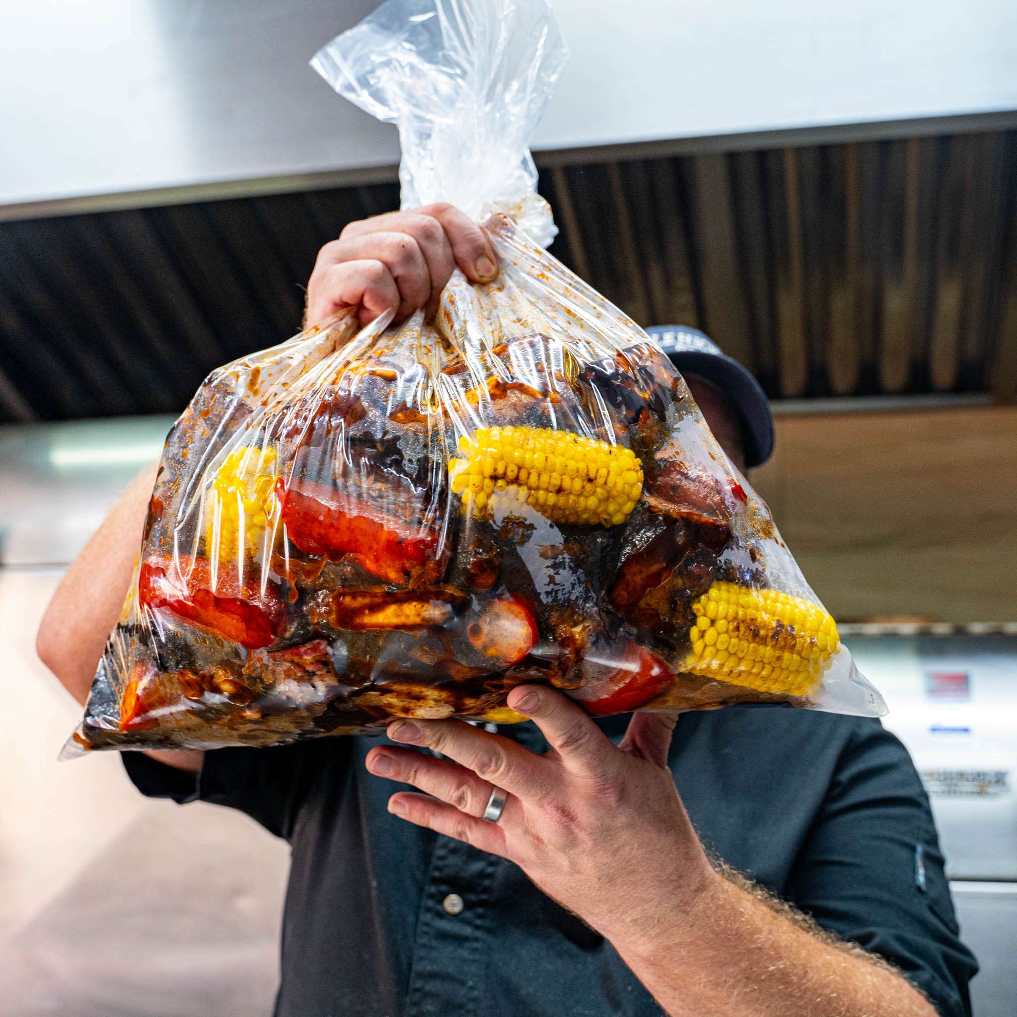 Hand holding a BBQ meat sack bag with ribs, corn and vegetables