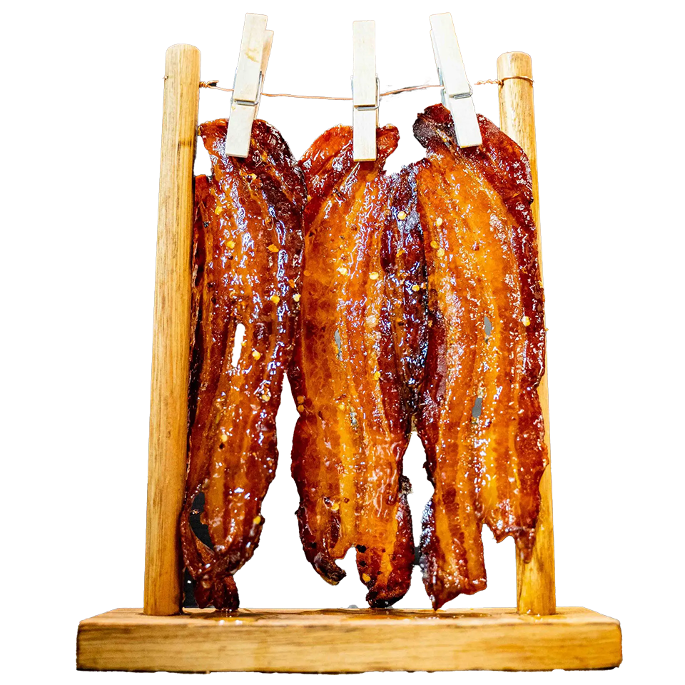 Candied bacon strips glazed and hanging to set on a wooden rack