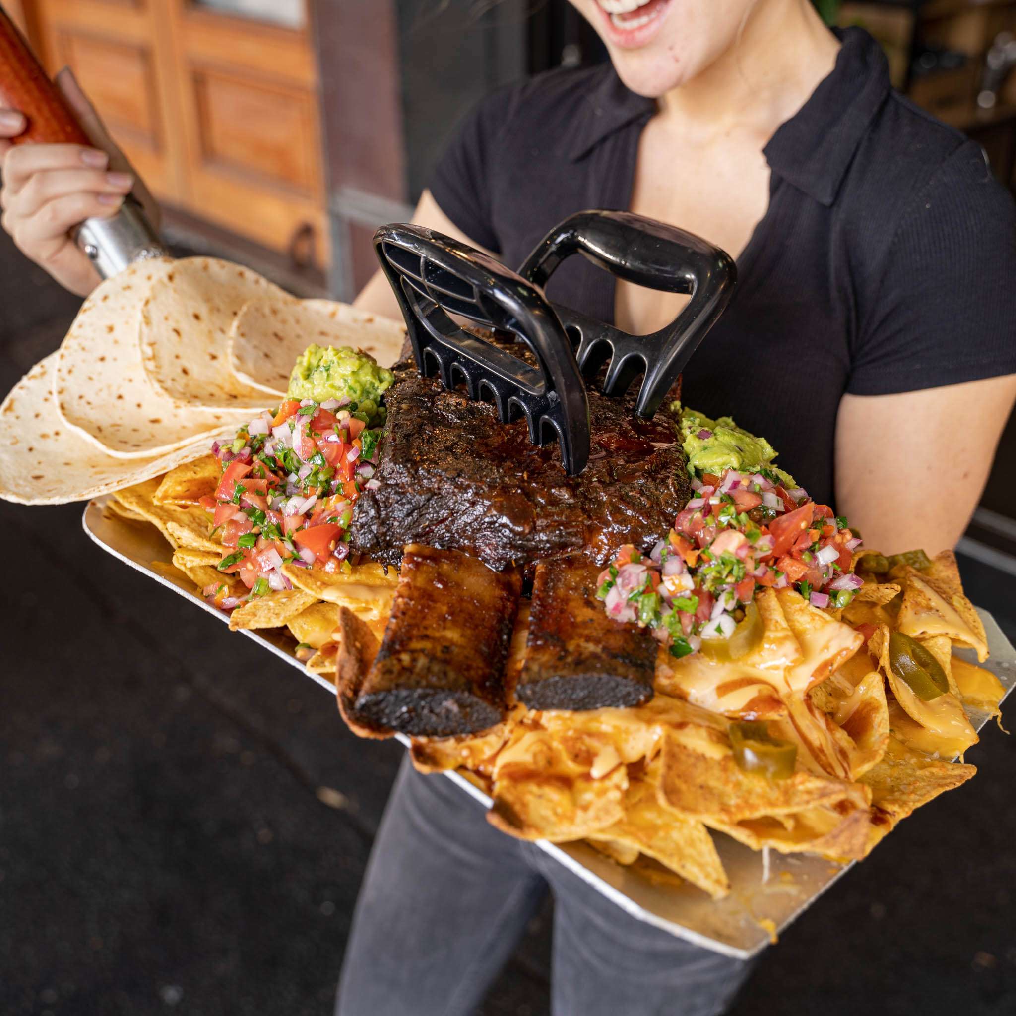 Person holding a nachos platter topped with a rib and guacamole