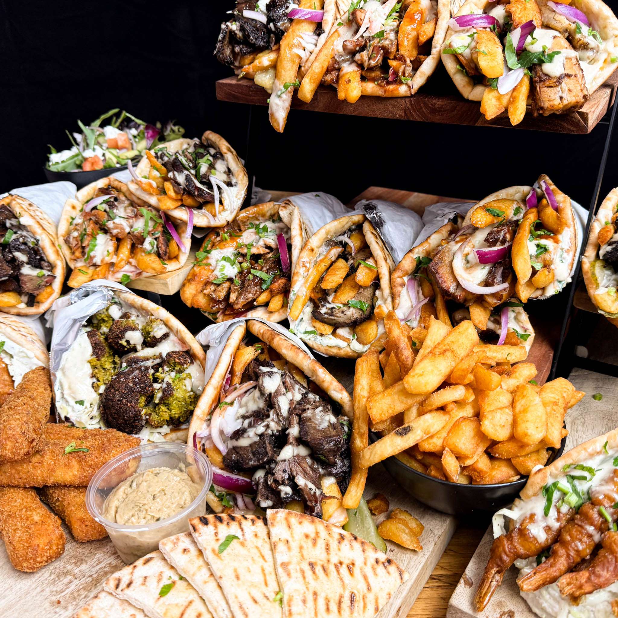 Selection of souvlaki wraps, loaded chips and dips on a board