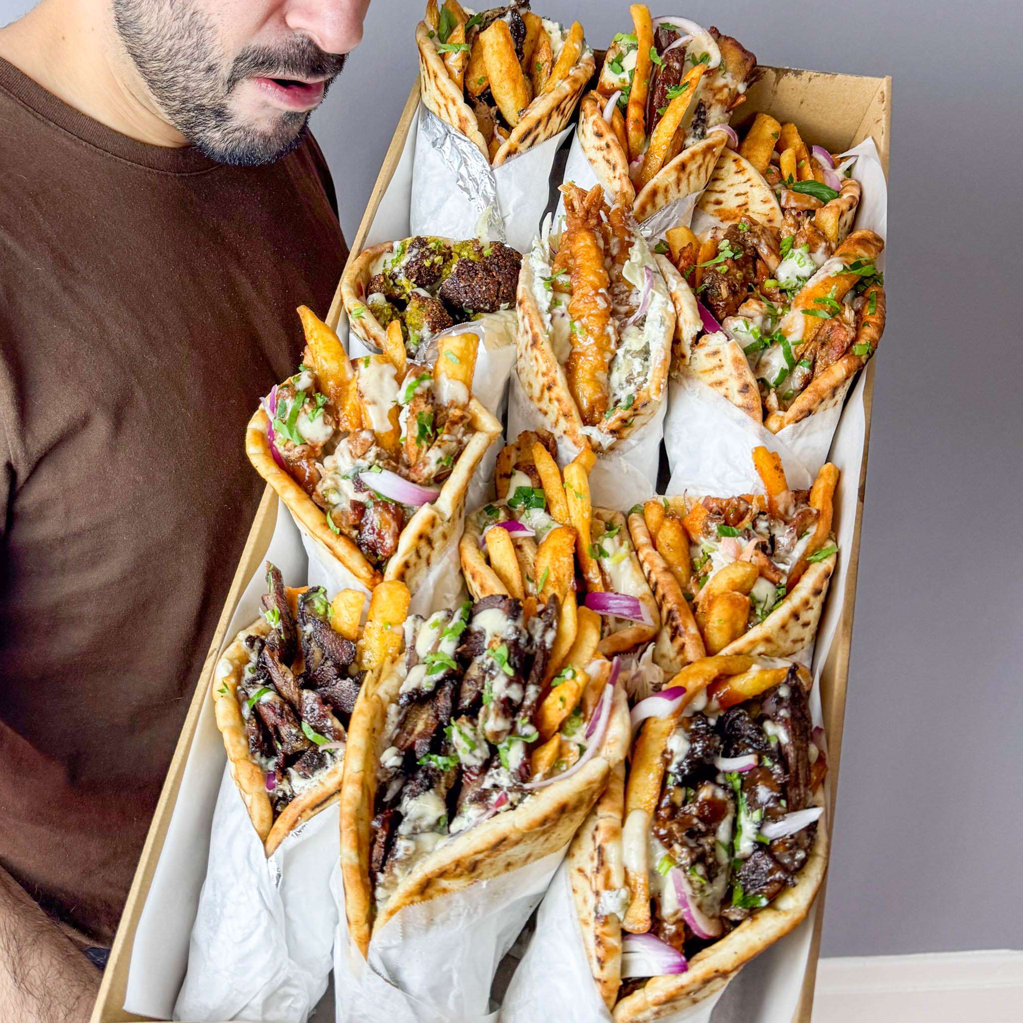 Person holding a tray of wrapped souvlaki and chips for catering