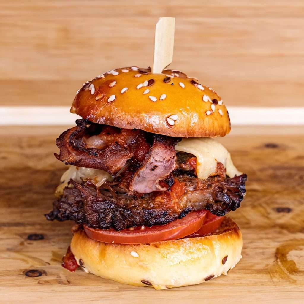 Loaded slider with smoked meat, bacon and tomato on a wooden board