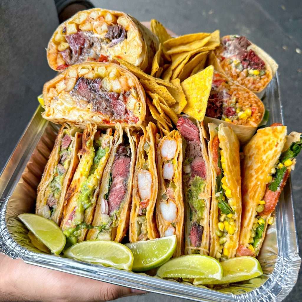 Hand holding a tray of assorted Mexican catering with lime wedges