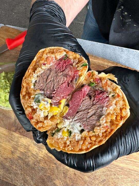 Halved beef quesadilla with corn and melted cheese, held up