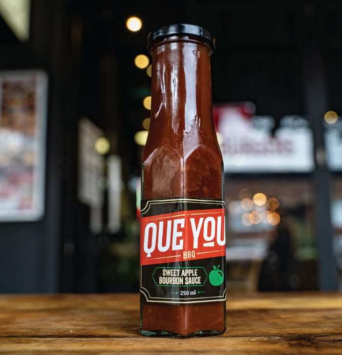 Que You Sweet Apple Bourbon Sauce bottle on a wooden table
