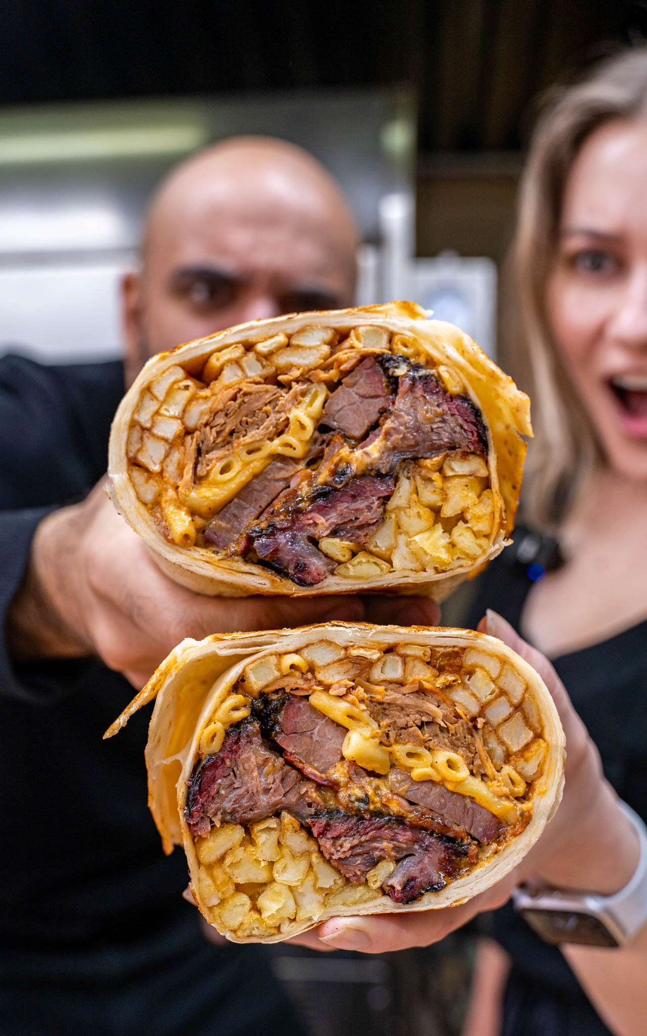 Two staff holding halves of the Everything Burrito filled with meat and cheese