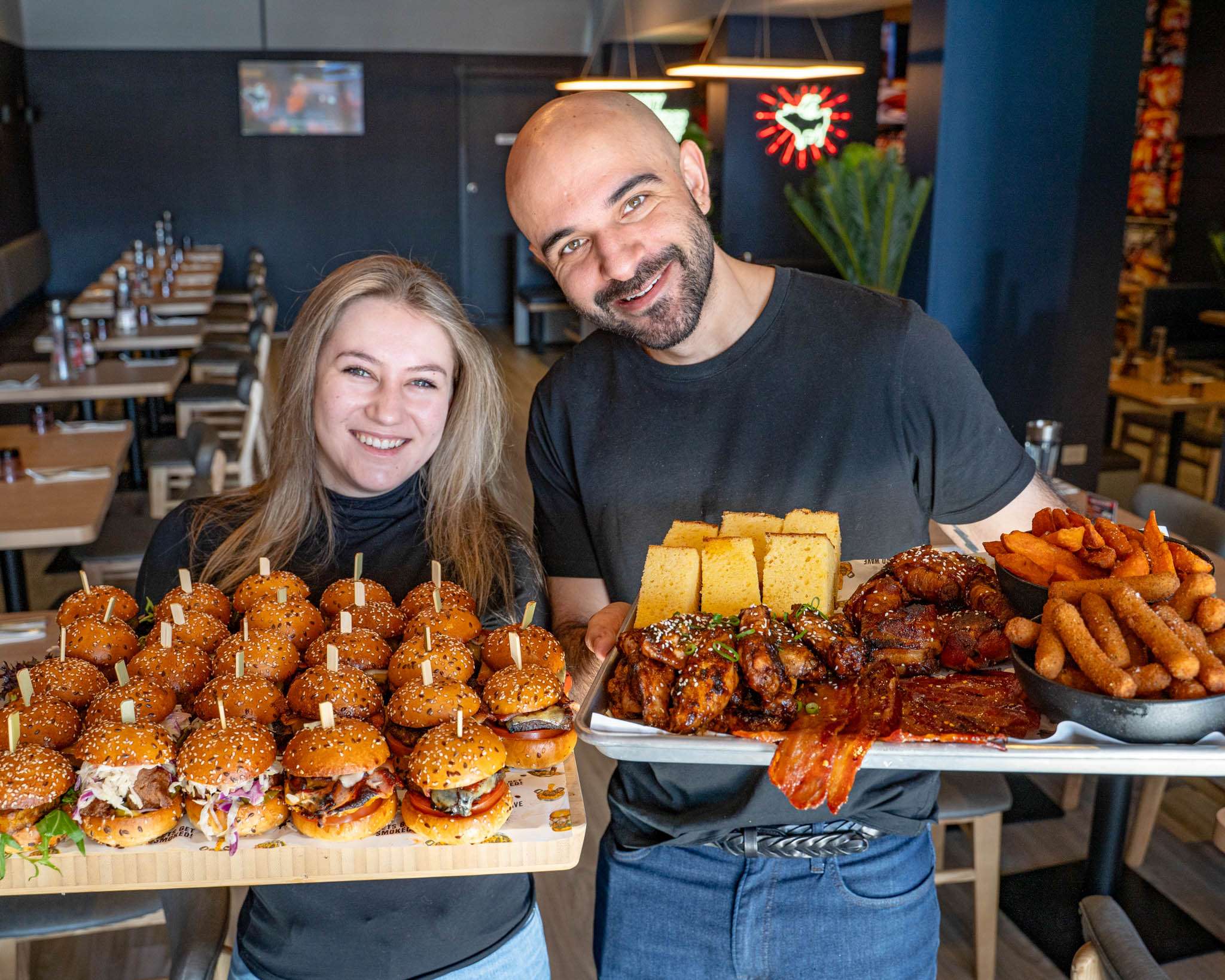 Two staff holding trays of sliders and smoked meats for a function at Third Wave BBQ