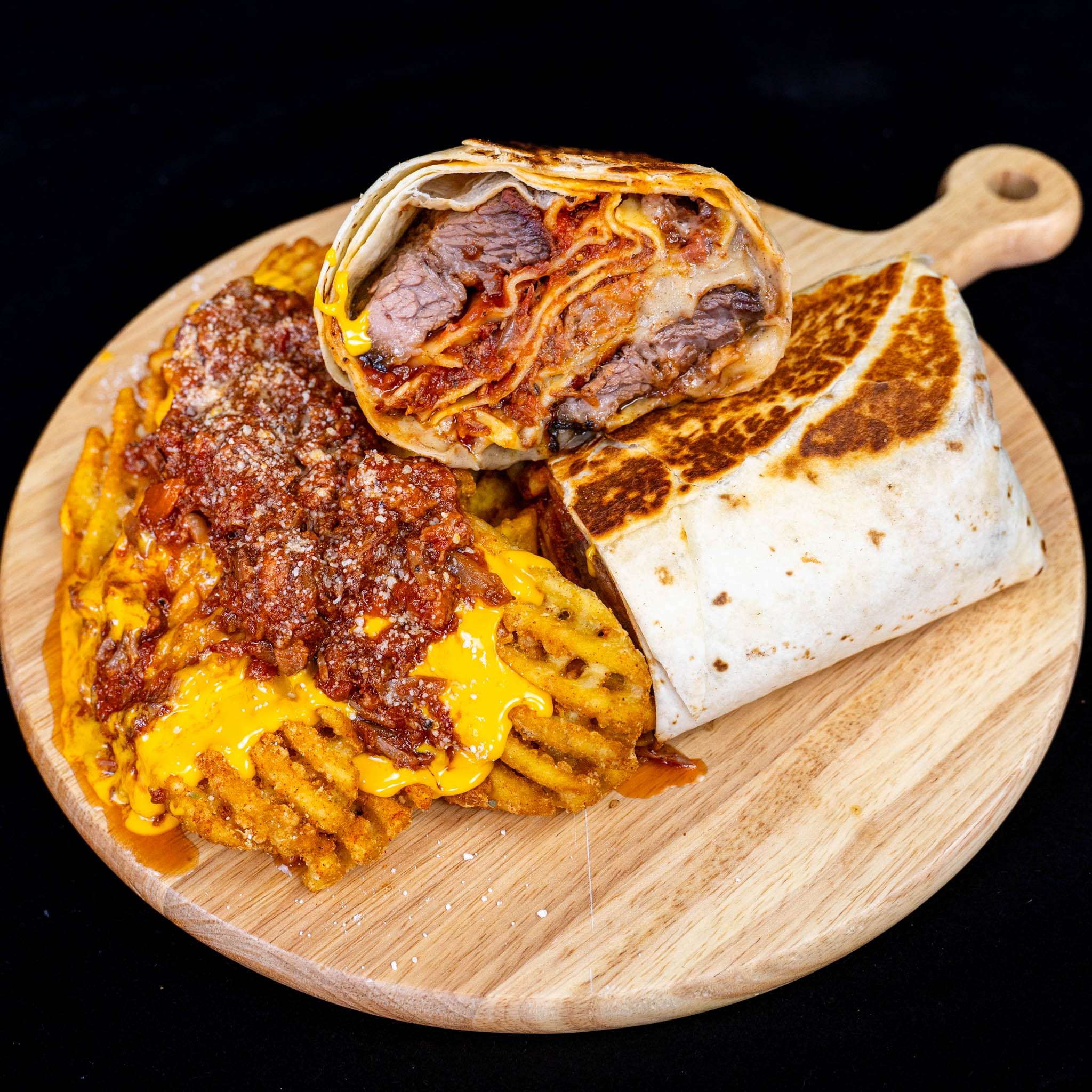Brisket lasagna burrito sliced in half next to loaded waffle fries