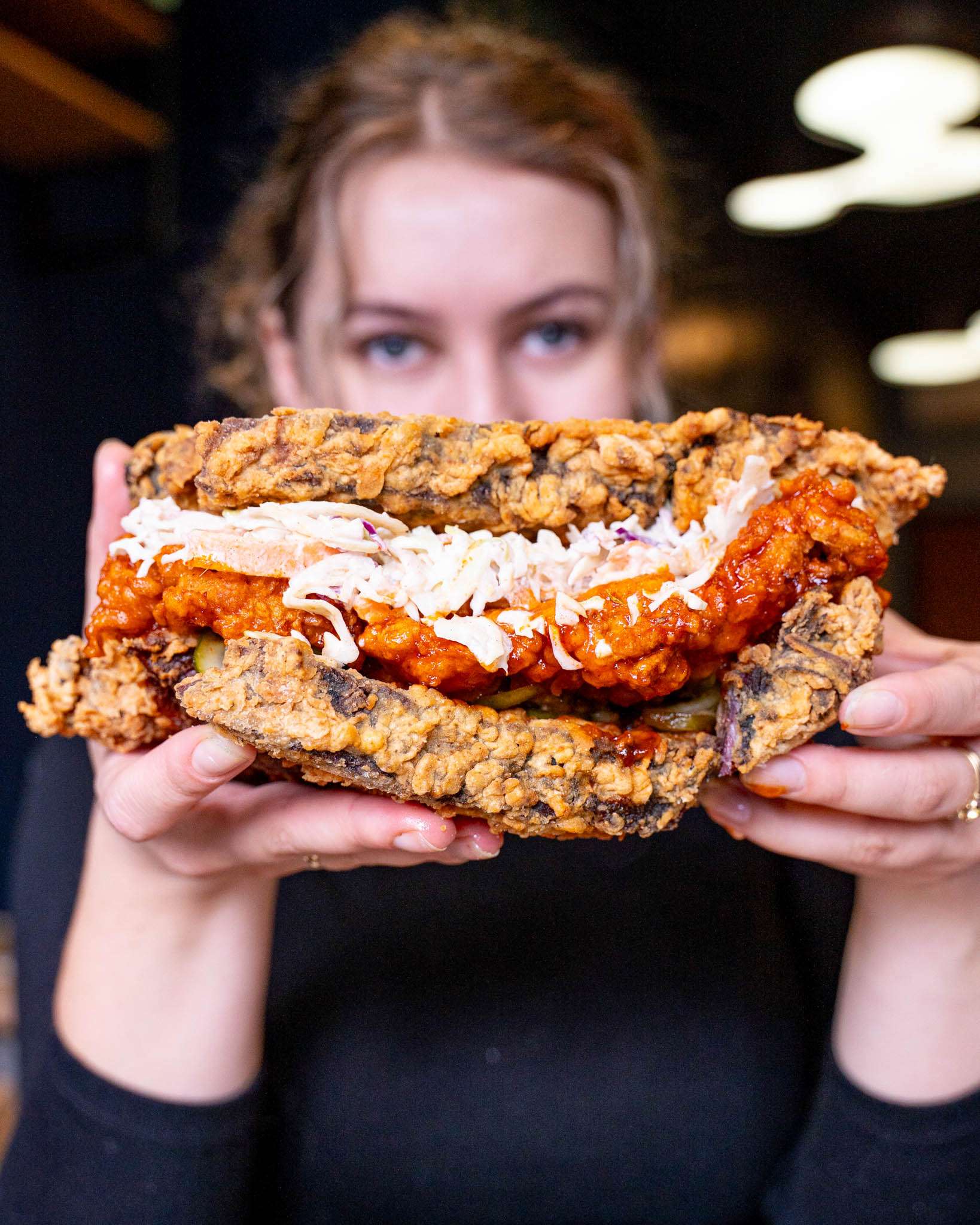 Diner holding a loaded sandwich with crispy coating and coleslaw