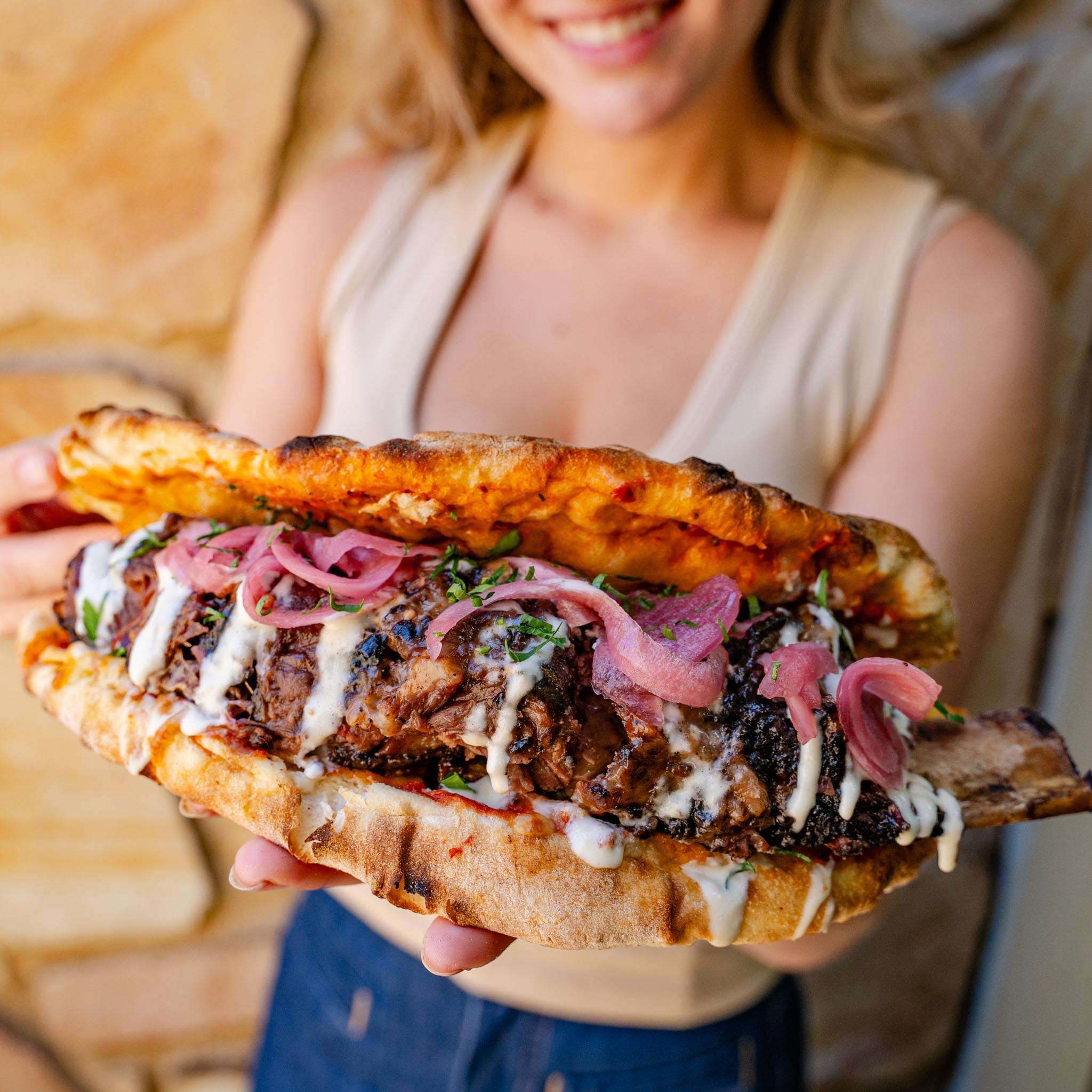 Person holding a 48-hour BBQ pizza pocket with pickled onion