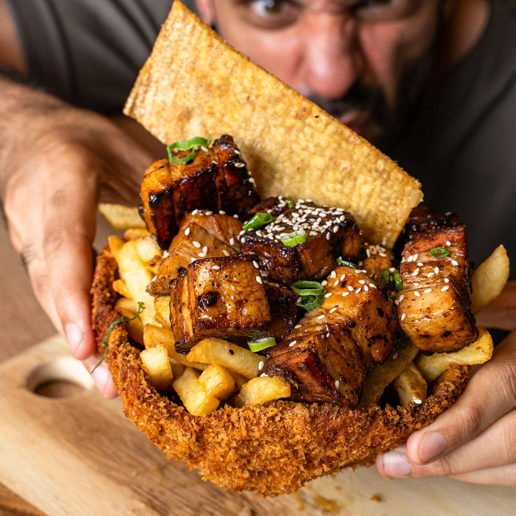 Crispy tortilla bowl filled with glazed meat, fries and sesame seeds, held by a guest