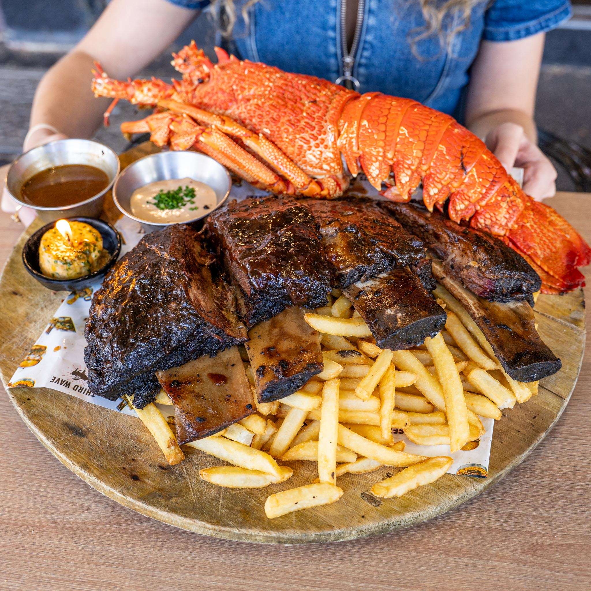 Lobster tail, ribs and fries on a plate, held up