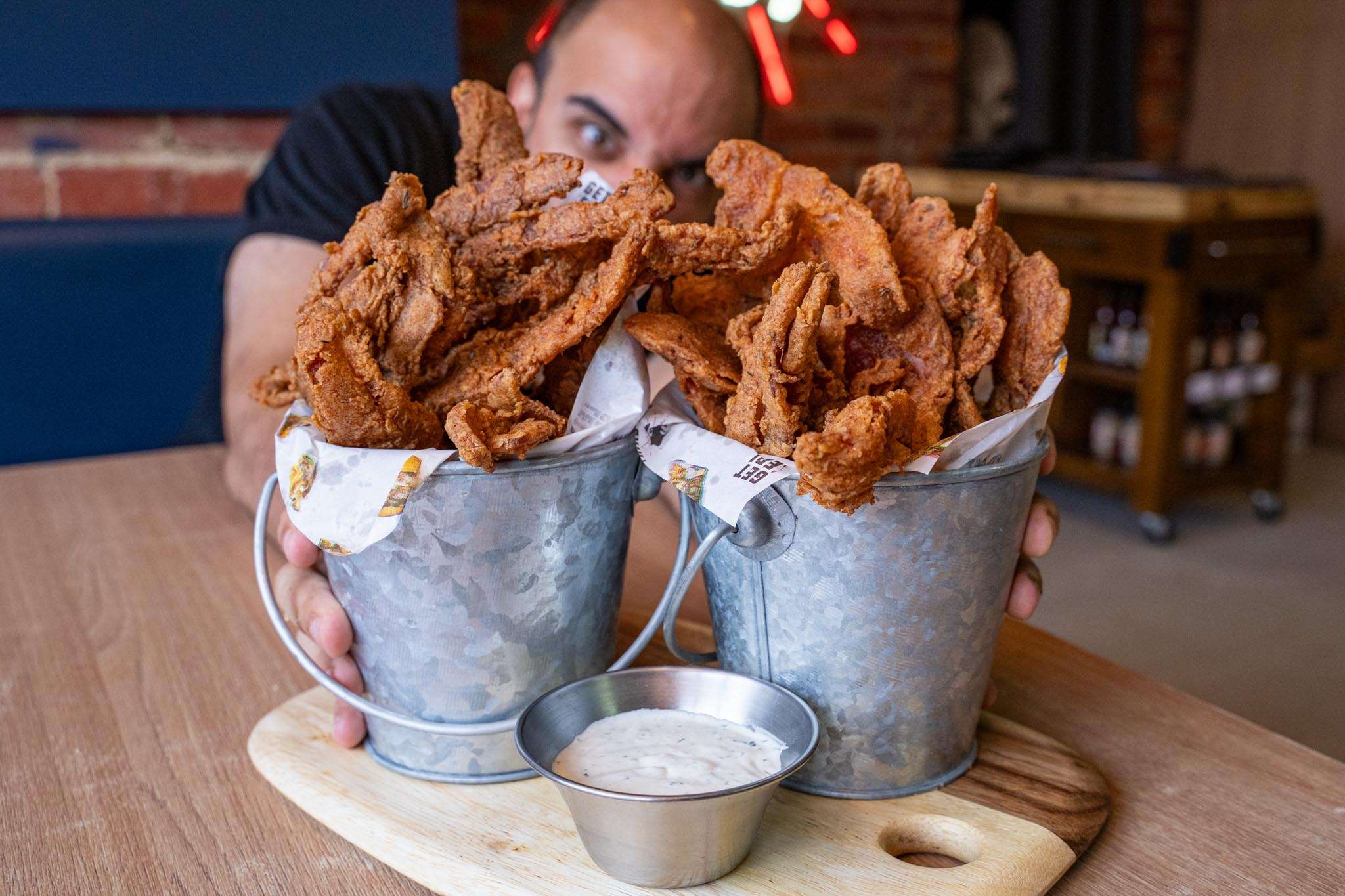Buckets of chicken fried bacon with a dipping sauce, held up