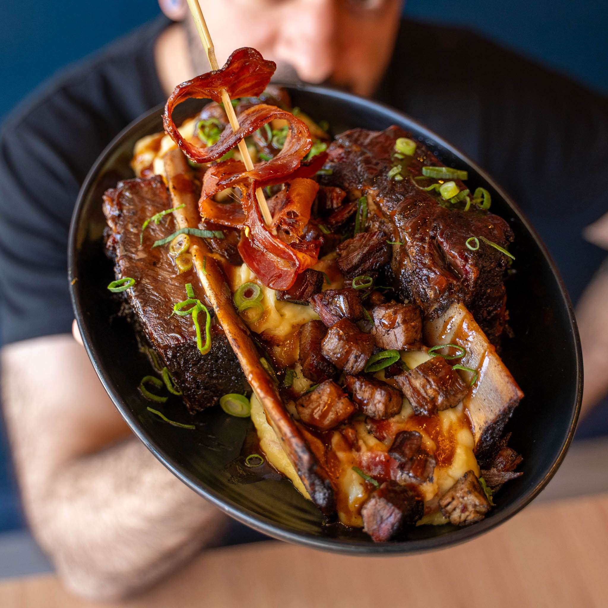 BBQ Banana Split dish held up, showing meat chunks and a bacon curl