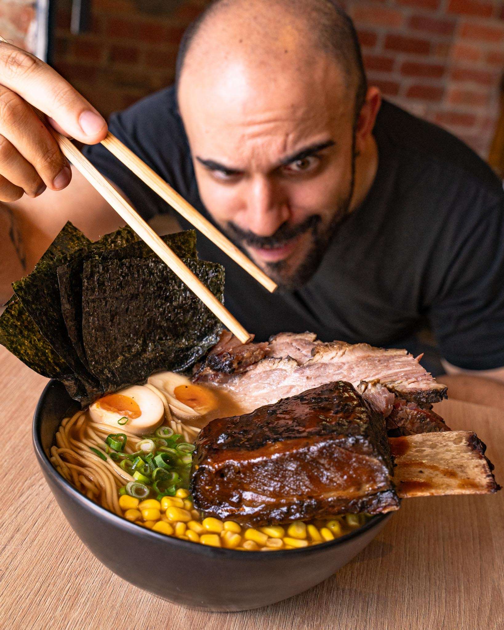 Guest eating a bowl of BBQ ramen topped with smoked brisket and nori