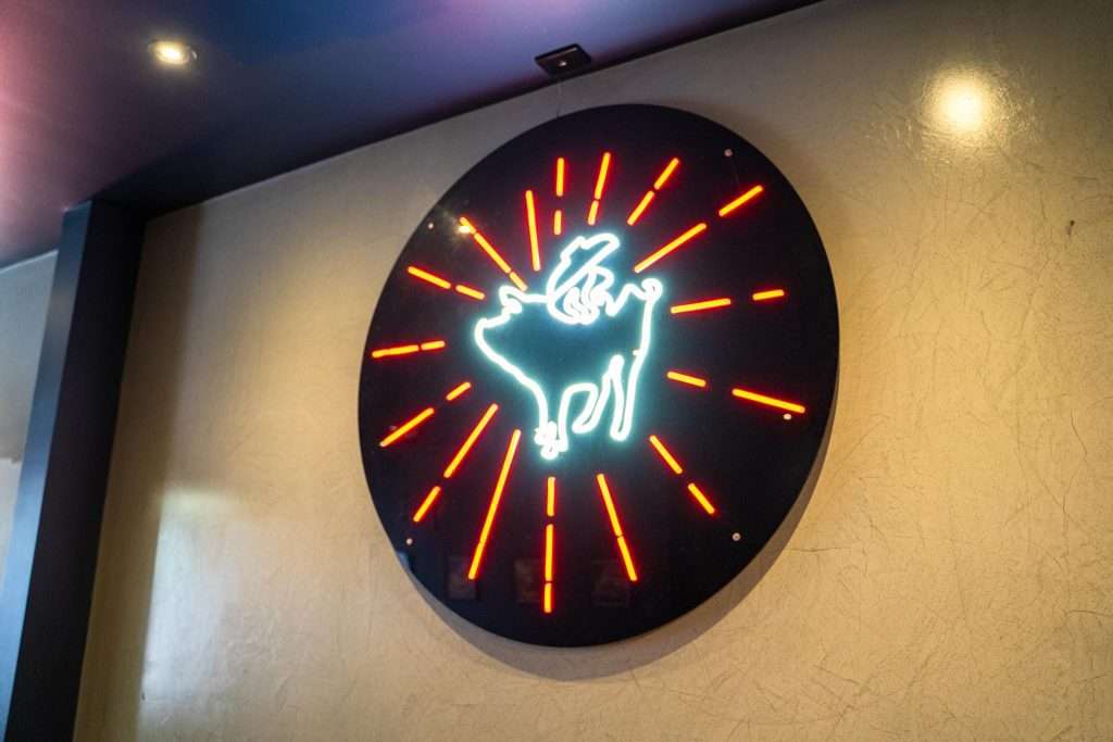 Neon sign of the Third Wave BBQ winged pig logo on a wall